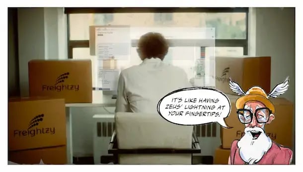 Person sitting in an office environment, looking at a computer screen with documents. There are two Freighty cardboard boxes. There is a cartoon character who is saying, 
